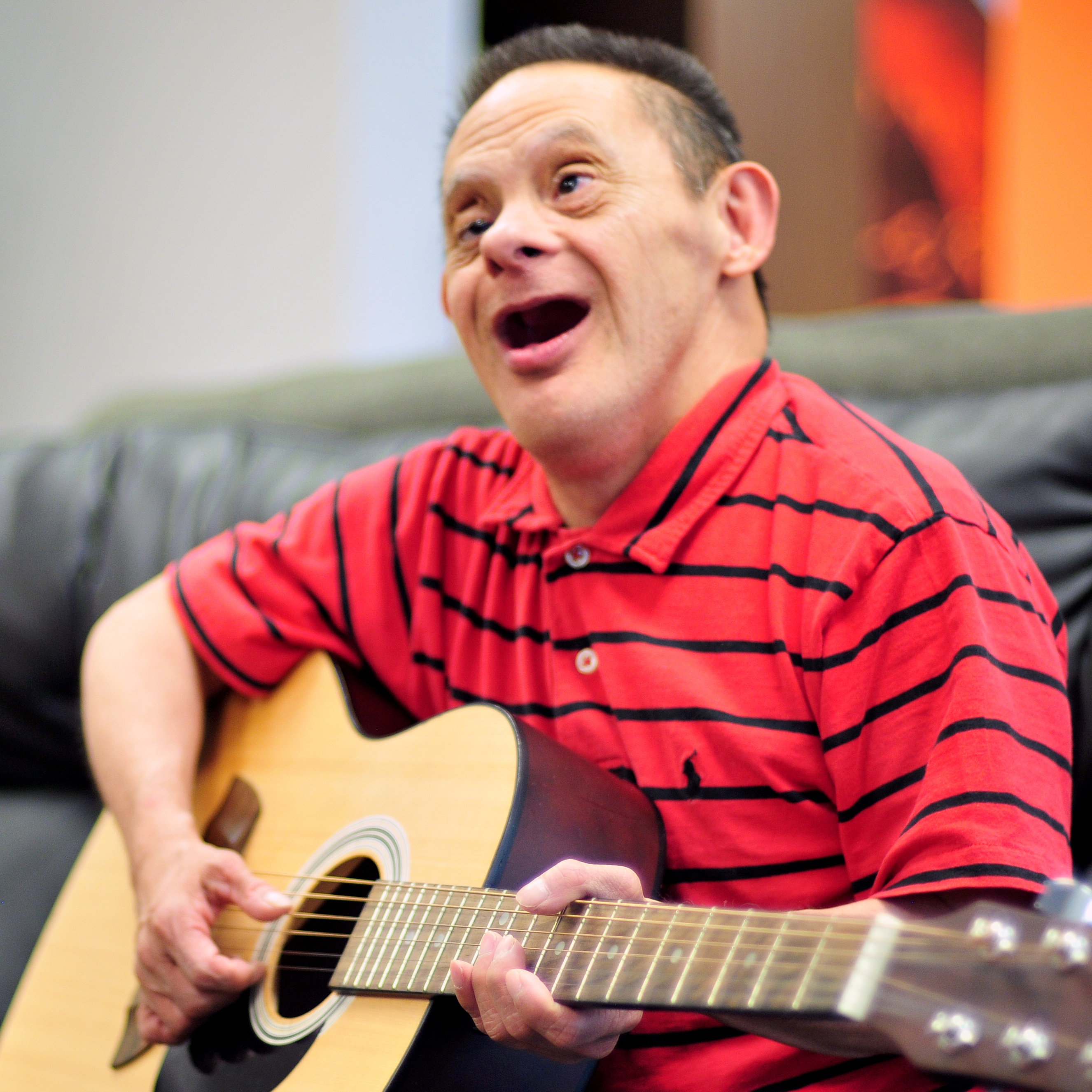 Man in red striped shirt playing guitar and singin