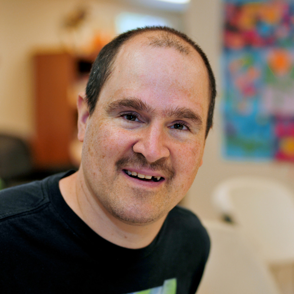 Man in short brown hair, a mustache and a black shirt grinning