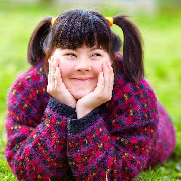 Smiling girl in pig tails with a burgundy sweater laying on the grass with hands on her face