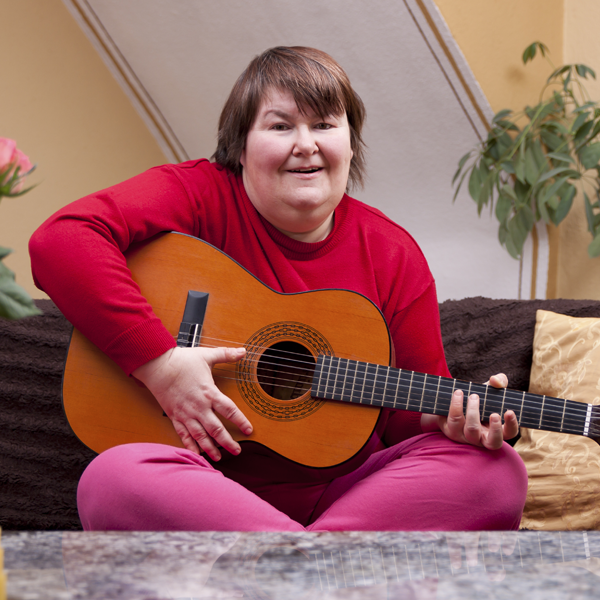 Woman in red shirt sitting with legs crossed playing a guitar