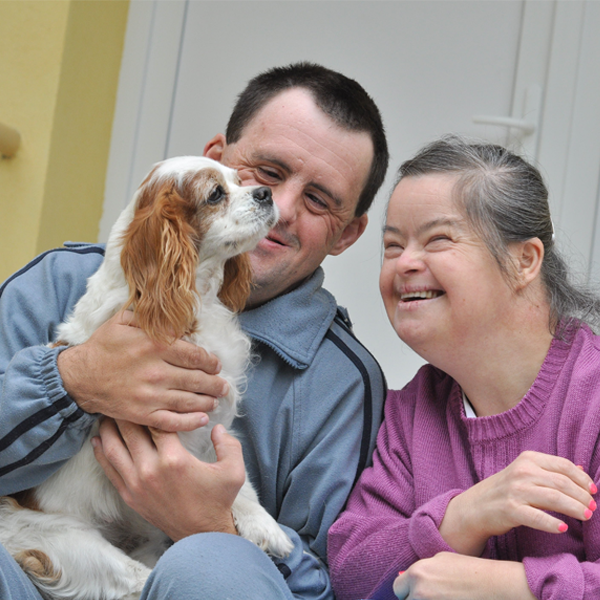 Man and woman smiling sitting next to each other with a dog on his lap